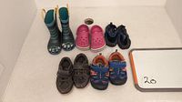 Overview of six pairs of kid's shoes including rain boots, crocs, water skippers, and casual shoes in various colors and sizes 5 to 7.