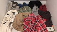 Photo showing over 20 men's tops including dress shirts, golf polo shirts, long sleeve casual shirts, and sweaters. Various colors such as red plaid, beige, white, green, blue, black, and striped patterns visible.