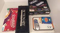 Photo shows boxed games including Scrabble, Pictionary, Wizard card game, a multi kit glass chess/checkers/backgammon set, and Pass the Pigs components.