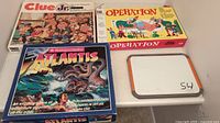 Photo showing three board game boxes: Clue Jr., Operation, and Atlantis with a whiteboard marked 54.