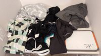 Photo showing seven pieces of boys sports clothing laid out, including one striped short sleeve shirt and six pairs of assorted shorts in dark and light colors.