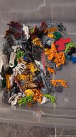 Loose mixed LEGO Technic and Bionicle pieces in assorted colors and shapes in a clear plastic container