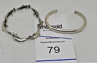 Two sterling silver bracelets shown together: one dolphin link bracelet and one plain cuff bracelet on a white surface with a lot card.