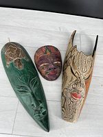Three Indonesian carved wood masks displayed on floor showing all three distinct masks.