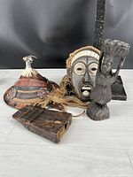 All four African souvenirs arranged on floor with black background: Tuareg hat, Congo mask, Cameroon figure, and kalimba finger harp