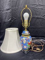 Full view of the Asian cloisonné small table lamp with off-white fabric lampshade beside it, showing lamp base, bulb, socket, and power cord.