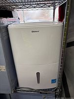 Front view of white Shinco dehumidifier showing water tank and brand label.