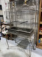 Front view of large ornate double iron birdcage on stand showing both cage compartments and ornate curved legs.