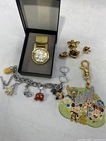 Photo displaying entire lot of Disney collectible accessories including money clip, charm bracelet, keychain, and pin backs.