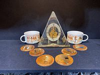 Full view of all nine items including Seiko pyramid clock, two Egyptian banquet mugs and six Egyptian-themed coasters grouped on black surface.