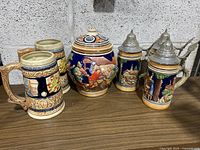 Photo of all five pieces showing two open beer steins, jar, and two pewter lidded steins.
