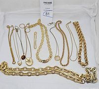 Overview of 11 goldtone jewelry pieces laid out including necklaces and bracelets with various pendants and chain styles.