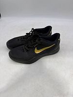 Side view of black and gold Kobe Bryant Nike basketball shoes showing design and color scheme.