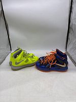 Side view of both LeBron 10 basketball sneakers shown side by side, Voltage in neon yellow and Galaxy Elite in metallic blue.