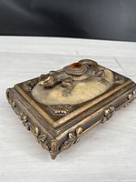 Front angle of rectangular trinket box with bronze finish and lizard motif on lid.