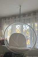 Front view of acrylic bubble chair with white seat and back cushion suspended by chain