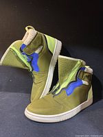 Pair of green Nike Air Jordan high-top sneakers with blue and neon green accents and shearling lining, photographed side view with tongue unfolded.