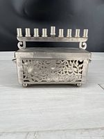 Front view of the silver-tone heavy gauge steel menorah with detailed cut-out patterns and candle holders on top.