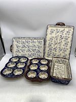 Full view of all five Temptations ceramic ovenware pieces showing two rectangular baking trays, two 6-cup cupcake trays, and a bread loaf pan with insert displaying blue floral patterns and brown edges with dotted white decoration.