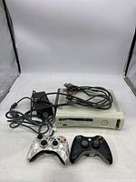 White Xbox 360 console with two wireless controllers and cables arranged in front.