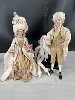 Three artisan dolls standing together against a black background, showing full view of costumes and faces.