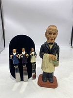 Full view of the vintage butler bottle opener figure next to three butler cheese spreaders on black velvet holder