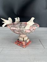 Front angled view of the vintage Italian marble compote with three white marble birds perched on the rim. Shows intricate carved leaf detail on rim and marbled pink and gray coloration.