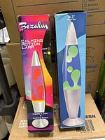 Two boxed vintage lava lamps side by side on a box, showing front packaging. Bezalm Calming Motion Lamp packaging features orange wax and pink-yellow background, Jambo Liquid Lamp packaging blue background with green wax.