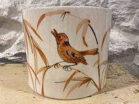 Front view showing brown bird on branch and grass design on white ceramic planter.