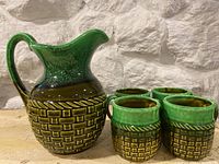 Front angle view of Japan pottery jug and four mugs arranged in front of textured stone wall.