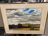 Framed landscape painting showing cloudy sky, fields, distant trees, and house. Signature visible.