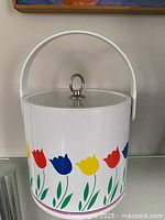 Large white ice bucket decorated with colorful tulip patterns and a lid with a metal loop handle, showing overall design and handle