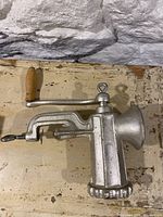 Side view of manual meat grinder with wooden handle, clamp, and grinding plate showing overall device shape and materials.