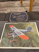 Photo of the airplane art print beside the scrapbook, showing the cover of the scrapbook and the full artwork of the airplane.