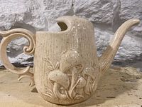 Side view of large tomato beige ceramic pottery pitcher with raised mushroom decoration and ornate handle