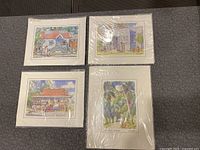 Four signed loose art prints laid out on carpet floor, depicting Barbados scenes