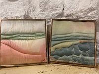 Pair of framed silk art pieces with abstract designs in soft gradient colors on a textured silk background, displayed side by side