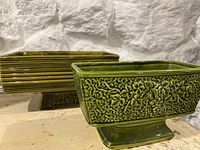 Two vintage Japanese ceramic planters with green glaze, one in front with floral and grapevine relief, and the other behind with ribbed linear pattern.