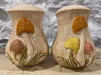 Front view of both mushroom salt and pepper shakers showing multicolored caps and detailed stems.
