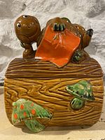 Front view showing the turtle on the log with mushrooms on front surface and turtle holding an orange leaf.