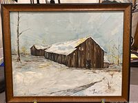 Framed oil painting showing rustic barn in winter snow, with trees in background and cloudy sky.