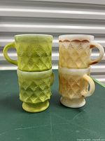 Two green and two yellow-brown Anchor Hocking Fire King Kimberly diamond milk glass mugs stacked and standing to show texture and colors.
