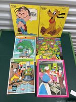 Lot of six vintage puzzles arranged on table, showing box illustrations including Linus, Pluto, TMNT, and Donald Duck.