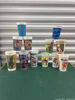 Full display of the 12 collectible plastic cups arranged in pyramid form showing a variety of designs from McDonalds, Burger King, Coca-Cola, and Pizza Hut with sports and film themes.