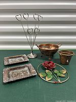 Lot of six metal and copper decor items shown on a green surface in front of a corrugated metal backdrop