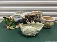 Photo showing five assorted flower pots including bird-themed planter, shell-shaped bowl, and other ceramic pots