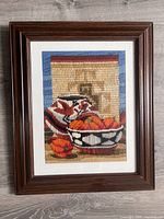 Front view of vintage needlepoint artwork framed, showing kitchen still life with bowl of pumpkins and pot.