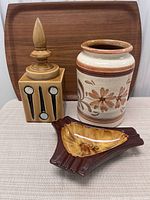Three vintage ceramic items: a square canister with finial lid and abstract black and white designs, round floral canister, and a mid-century style red ware ashtray.