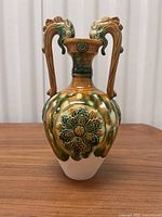 Front view of vintage Chinese porcelain urn showing ornate dragon head handles, tri-colour glaze in brown, green and cream, and raised floral medallion design.