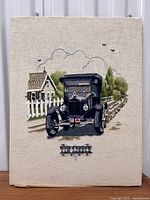 Full view of vintage crewel needlepoint showing black Ford Model T Tin Lizzie with house and white fence background on unframed fabric canvas.
